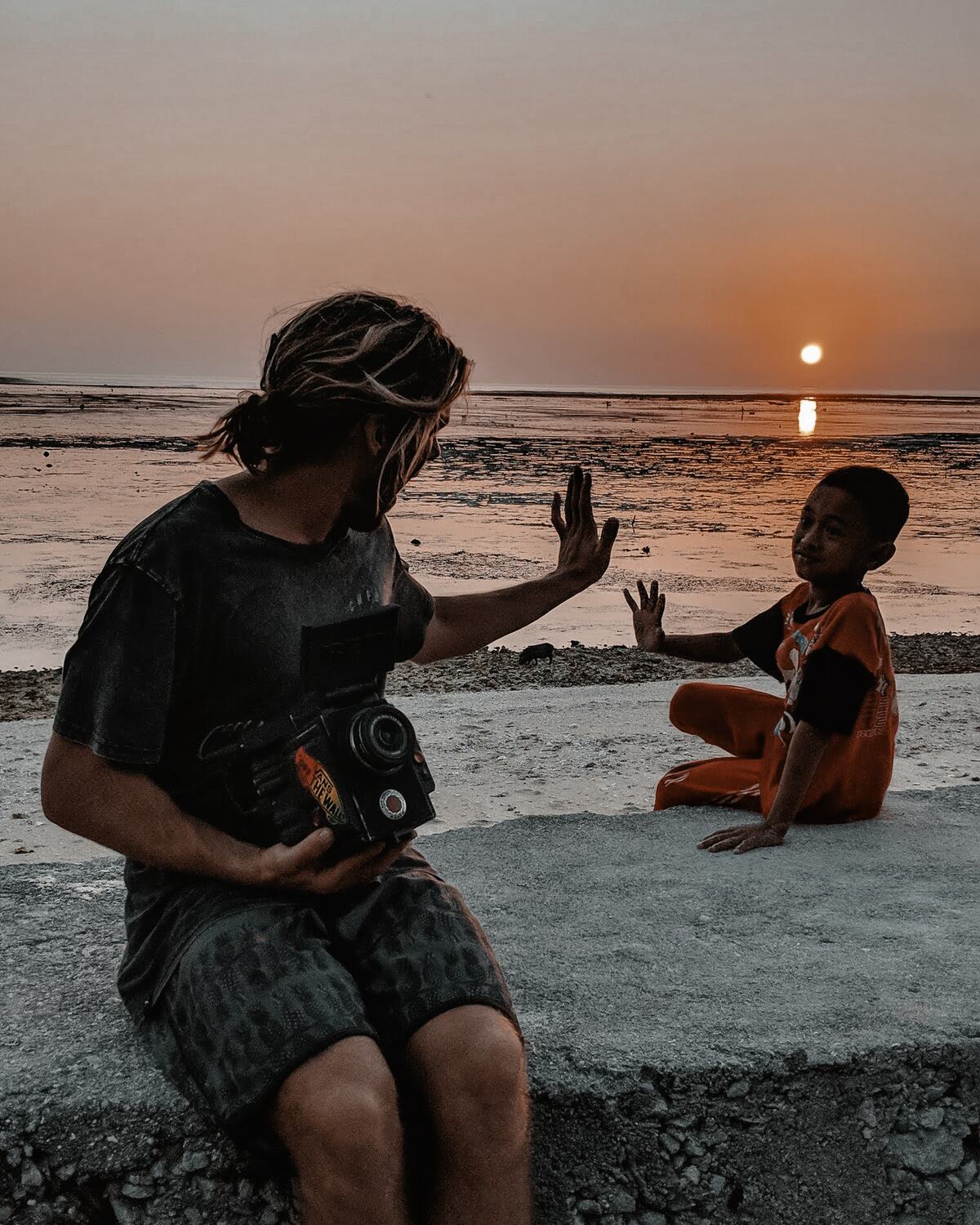 A filmmaker at work with a local child on the sand at sunset, Rote